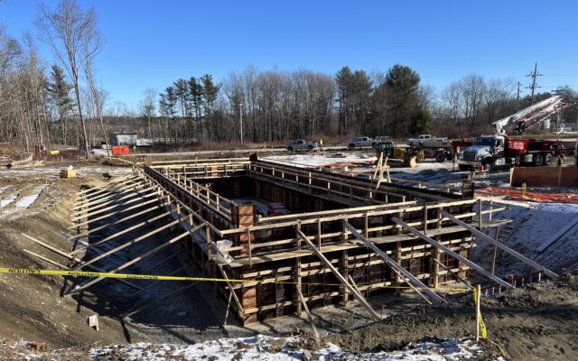 Wooden formwork at construction site with tape, cars, trees.