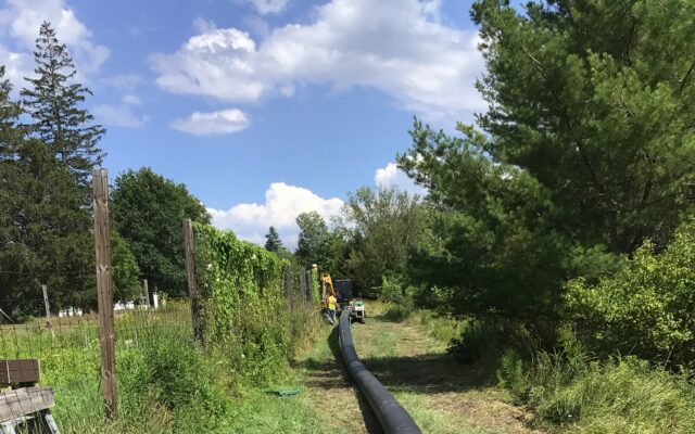 Black pipe with yellow cap on grass; workers in distance.