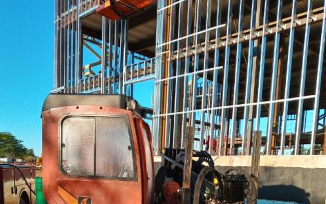 Damaged truck cab with exposed engine on sandy ground, construction nearby.