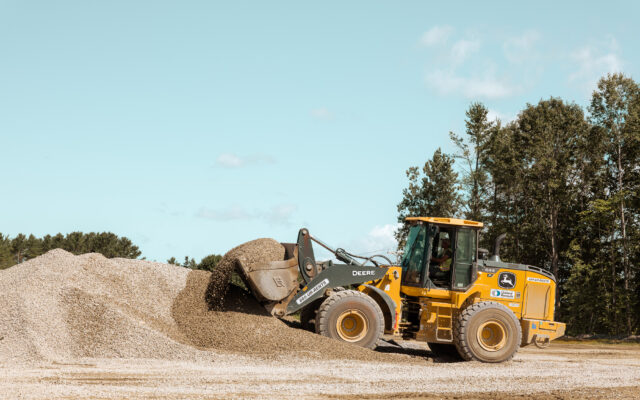 A construction vehicle is dumping gravel from a large pile onto the ground at a work site.