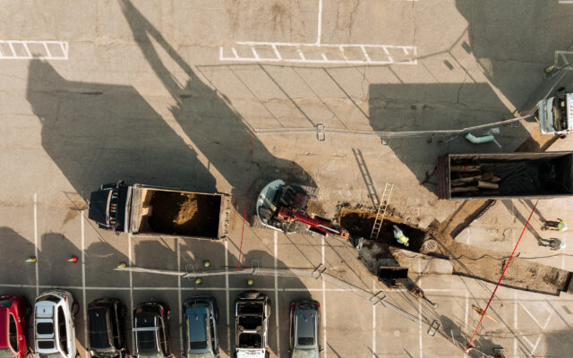 The image depicts a construction site with heavy machinery performing excavation work while several workers are present around the site.