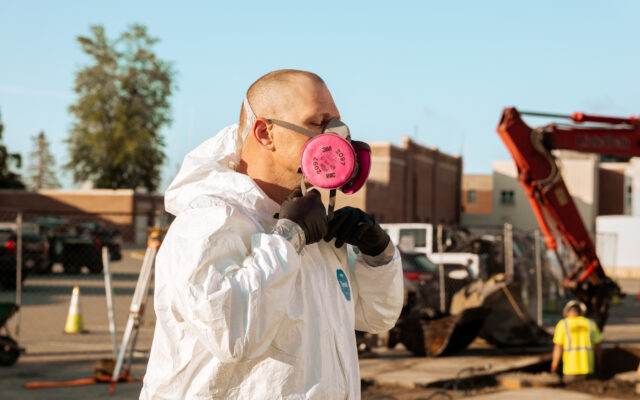 A worker prepares for a task by adjusting their protective mask while standing in a construction site environment.