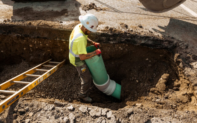 A construction worker is installing a green pipe into a trench at a construction site.