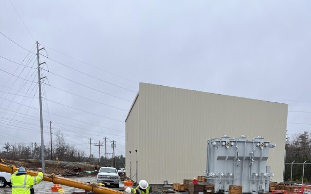 Workers in safety gear survey a muddy site with traffic barrels.