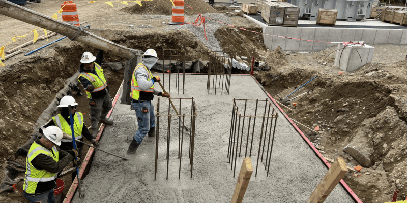 Four workers in safety gear level concrete in a rebar foundation.