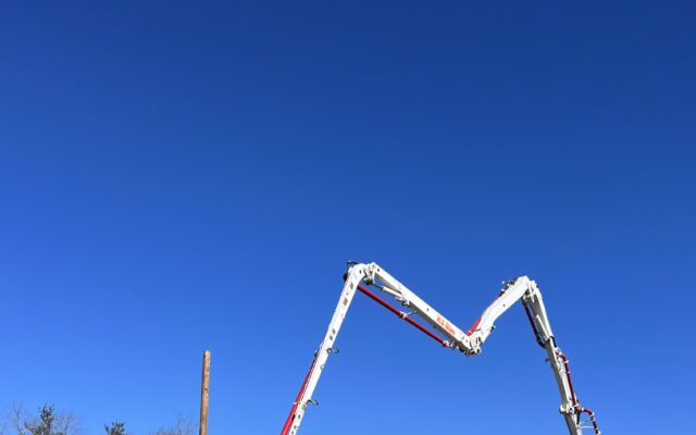Workers use a concrete pump truck at a roadside construction site.