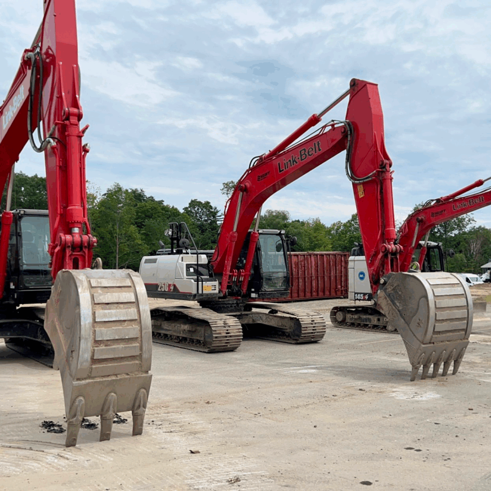 Three red excavators with raised buckets at a construction site.