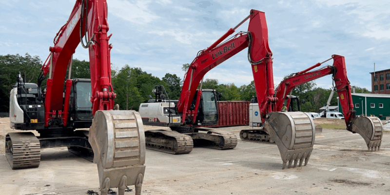 Three red excavators with raised buckets at a construction site.