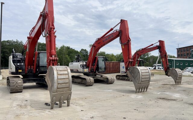 Three red excavators with raised buckets on a construction site.