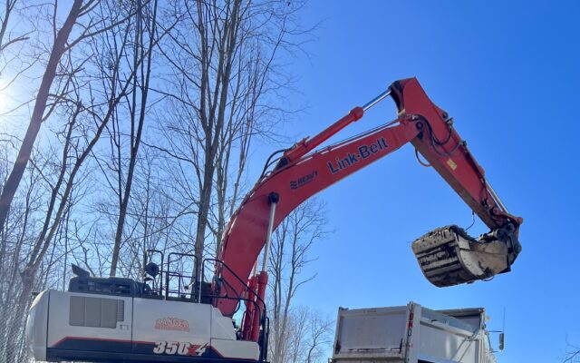 Excavator loads dirt into white dump truck at construction site.