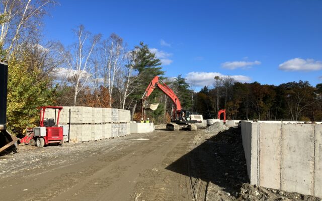 Construction site with road, barriers, blocks, excavators, and trees.