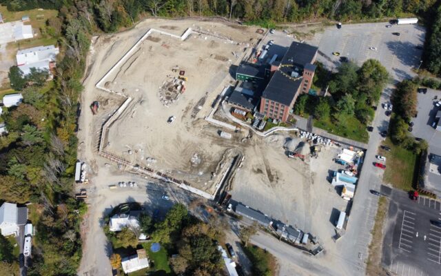 Aerial view of building foundations by brick building and trees.