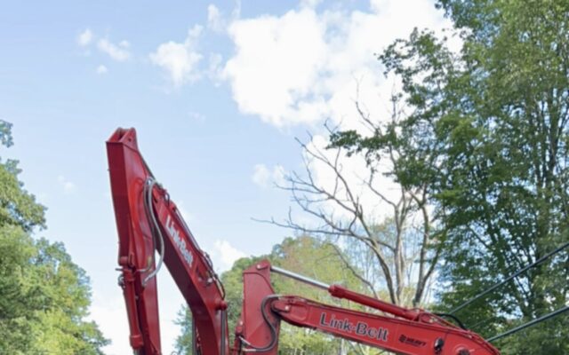 Workers with excavators near open trench, ladder, pipes, speed sign.