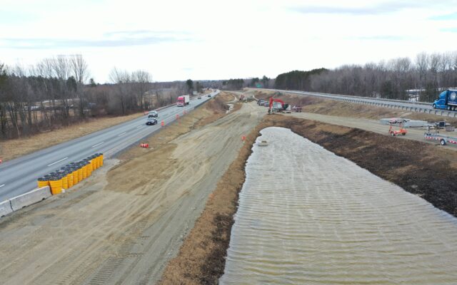 Construction site with vehicles, machinery, and large water-filled pit.