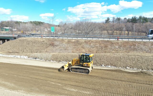 Yellow bulldozer leveling dirt at roadside construction site.