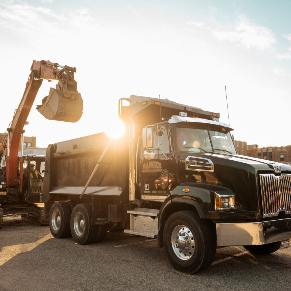 Black dump truck by excavator at sunrise, workers nearby.