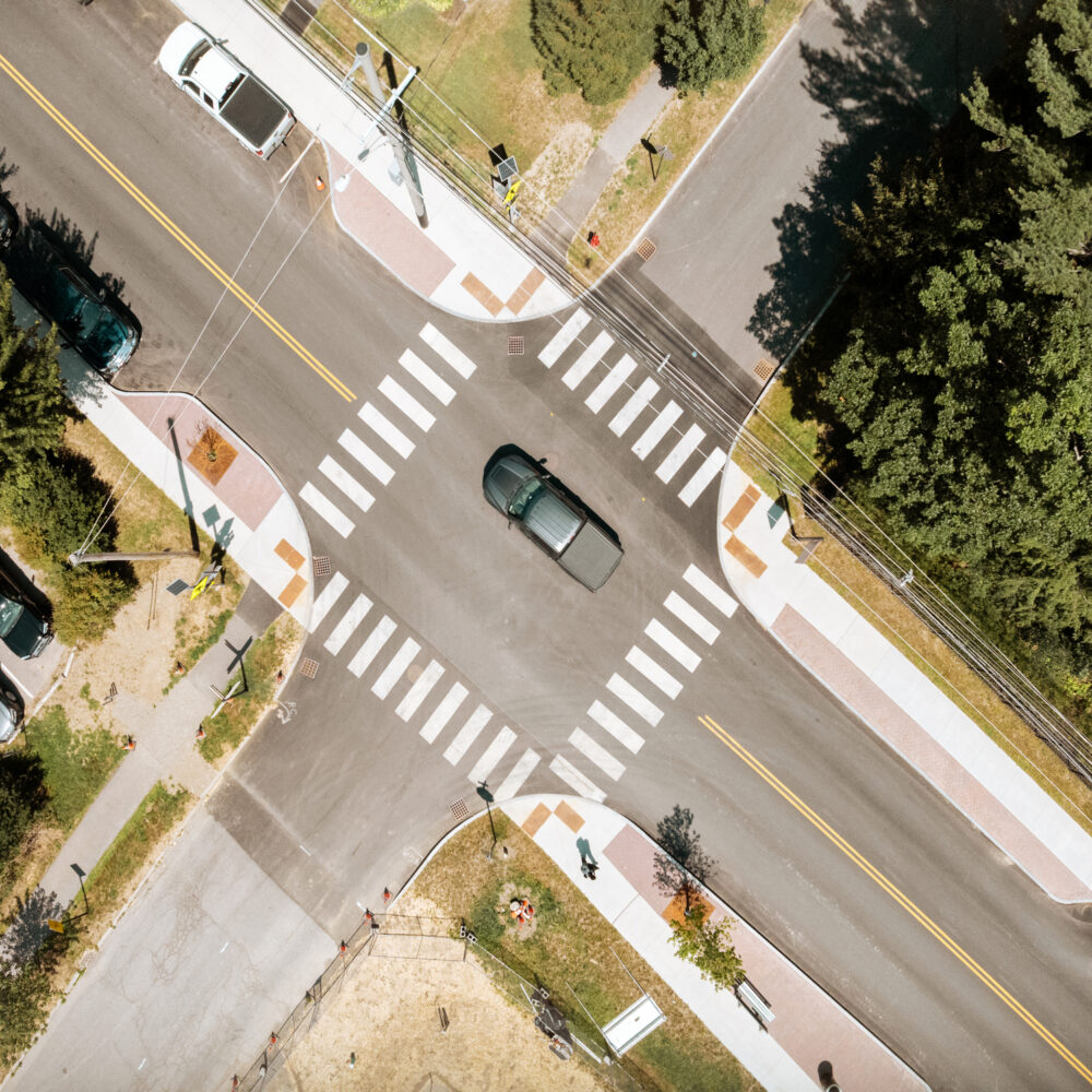 Car stopped in a crosswalk at a tree-lined intersection.