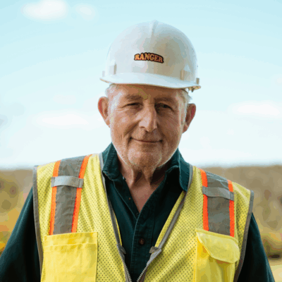 Older man in yellow vest and Ranger hard hat outdoors.