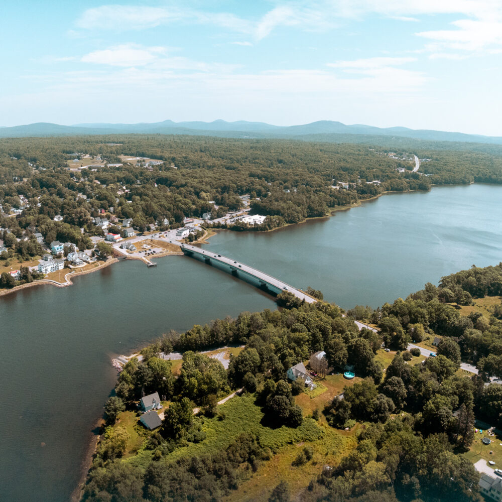 Aerial view: bridge over water, trees, houses, distant hills.
