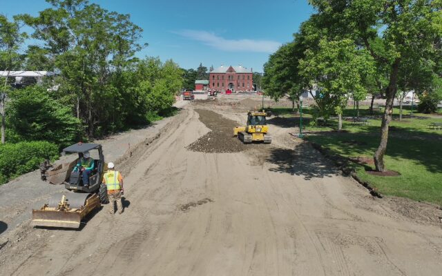 Workers and heavy machinery leveling dirt road at construction site.
