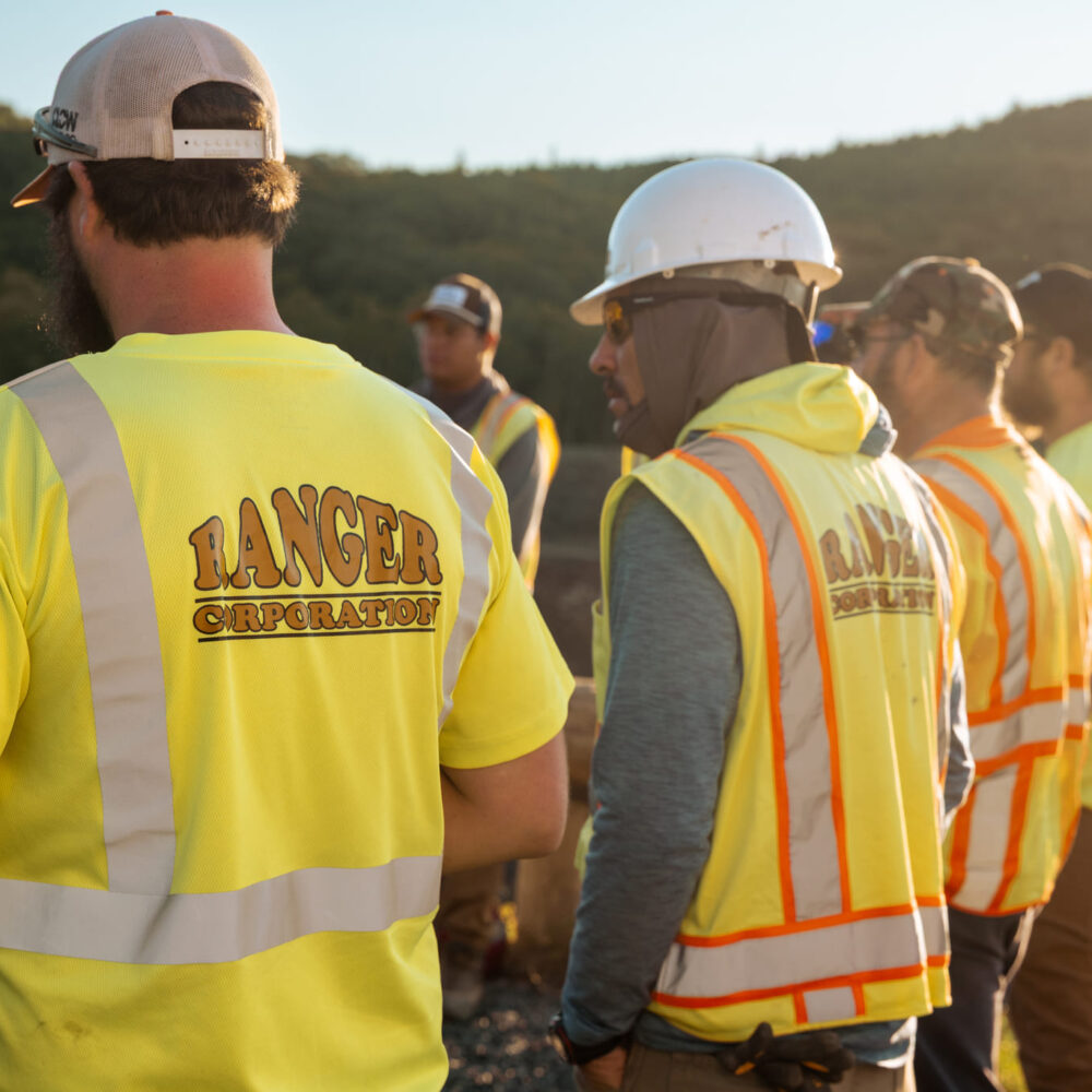 Construction workers in safety gear gather by a truck.