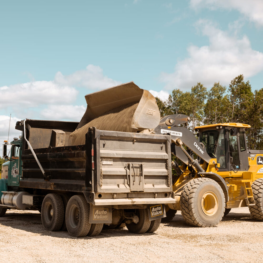 Yellow loader dumps sand into black dump truck.