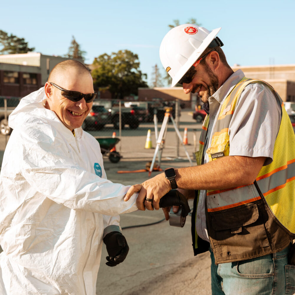 Two men in safety gear shake hands and smile on-site.