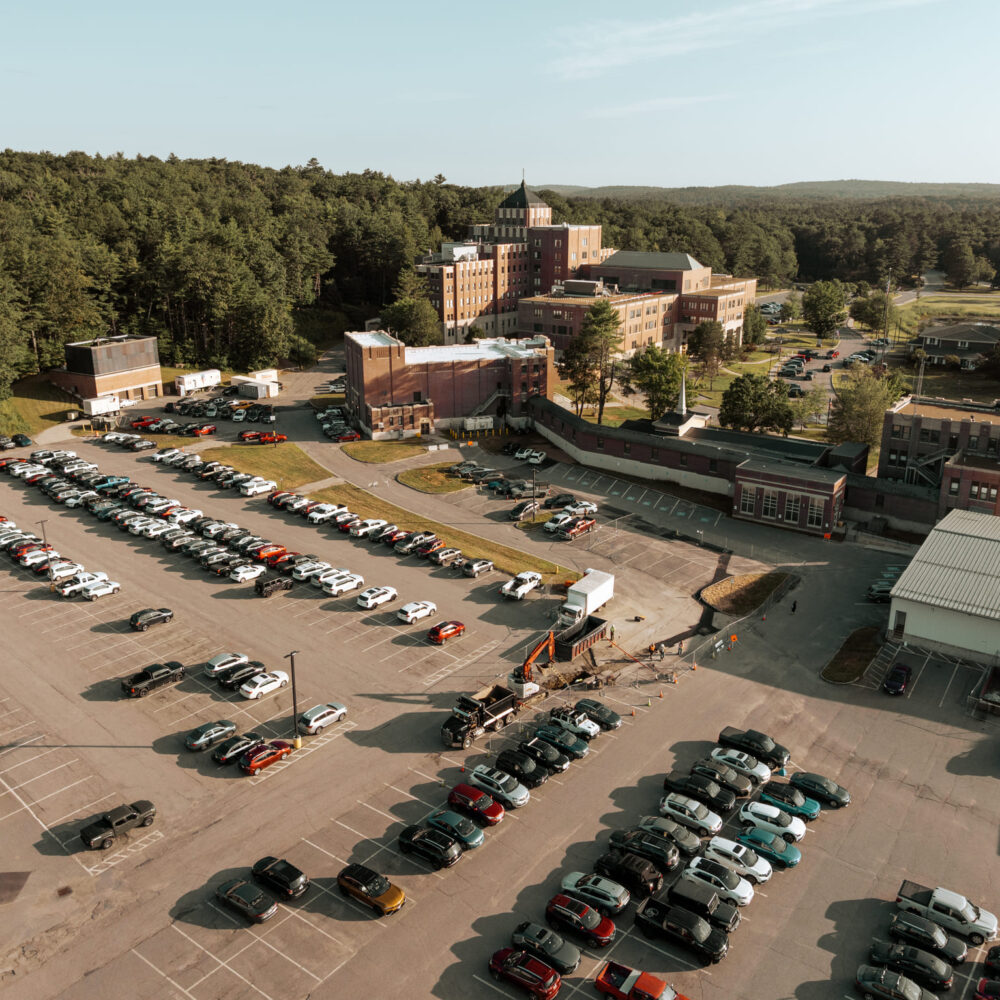 Aerial shot of crowded parking lot beside tall buildings and trees.