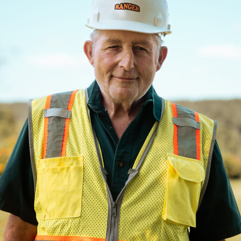 Older man in RANGER hard hat and yellow vest outdoors.