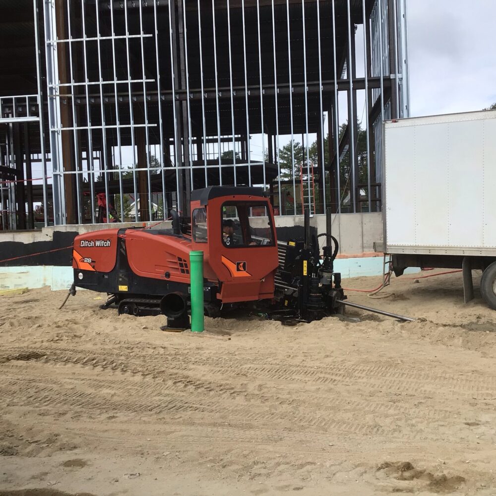 Orange Ditch Witch and white truck at construction site.