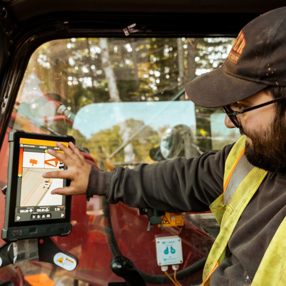 Person in safety vest uses tablet inside vehicle, trees outside.