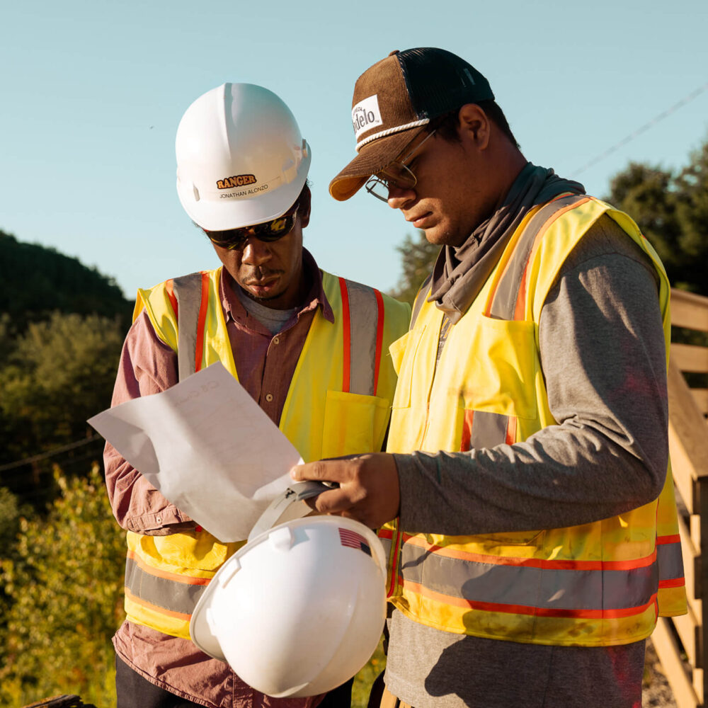 Two construction workers review documents outdoors at job site.