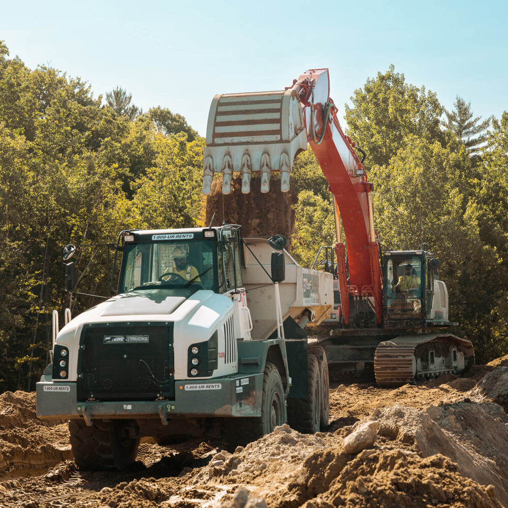 Red excavator loads soil into white dump truck outdoors.