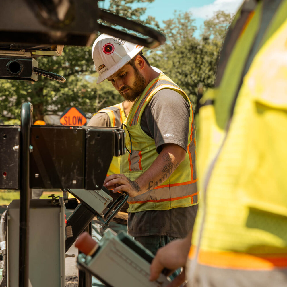 Worker in hard hat operates machinery near SLOW road sign.