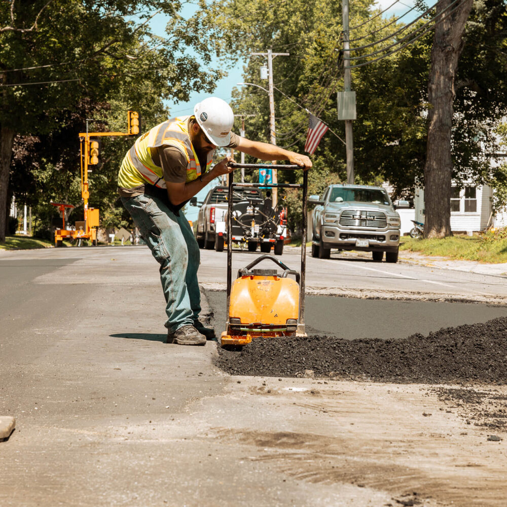 Worker in vest and helmet using compactor on new asphalt.
